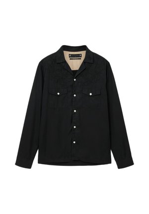 Schwarzes Langarmhemd mit besticktem Detail auf den Schultern, zwei Brusttaschen und quadratischen silbernen Knöpfen entlang der Vorderseite.