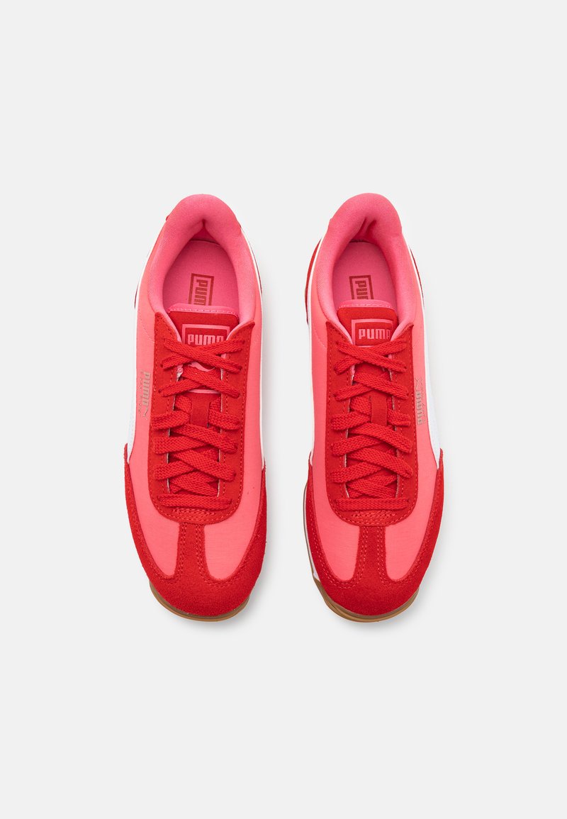 Baskets de sport rouges avec une tige en tissu doux et des accents en daim, lacets texturés et intérieur rembourré rose. Détail du logo blanc sur le côté.