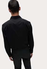 Zwarte langsl sleeve shirt met een klassieke kraag, een gladde textuur en knoopmanchetten, gecombineerd met donkergrijze broeken met achterzakken.