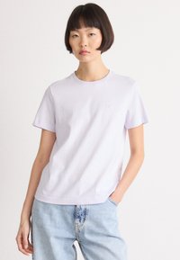 Lyse lilla bomulls-T-skjorte med korte ermer og rund hals. Har diskret "ck"-merke på brystet. Kombinert med lyseblå denimjeans.