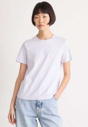 Lichtpaarse katoenen T-shirt met korte mouwen en een ronde hals. Heeft subtiele "ck" branding op de borst. Gepaarde met lichtblauwe denim jeans.