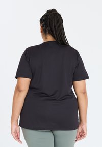 Sort kortærmet T-shirt lavet af blødt, strækbart materiale. Enkel design med rund halsudskæring. Bagfra viser den en glat silhuet.