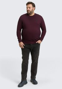 Bordeaux geribbelde trui met een ronde hals en zwart logo patch, gecombineerd met donkere jeans en marineblauwe sneakers, met een recht model.