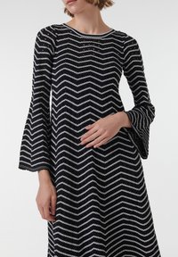 Vestido de chevron en blanco y negro con escote redondo y mangas de campana, que presenta una tela texturizada y una silueta fluida.