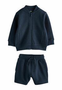 Mørkeblå strikket træningsdragt med en zip-up jakke, der har to sidelommer, ribbede manchetter og matchende shorts med elastisk talje og snøre.
