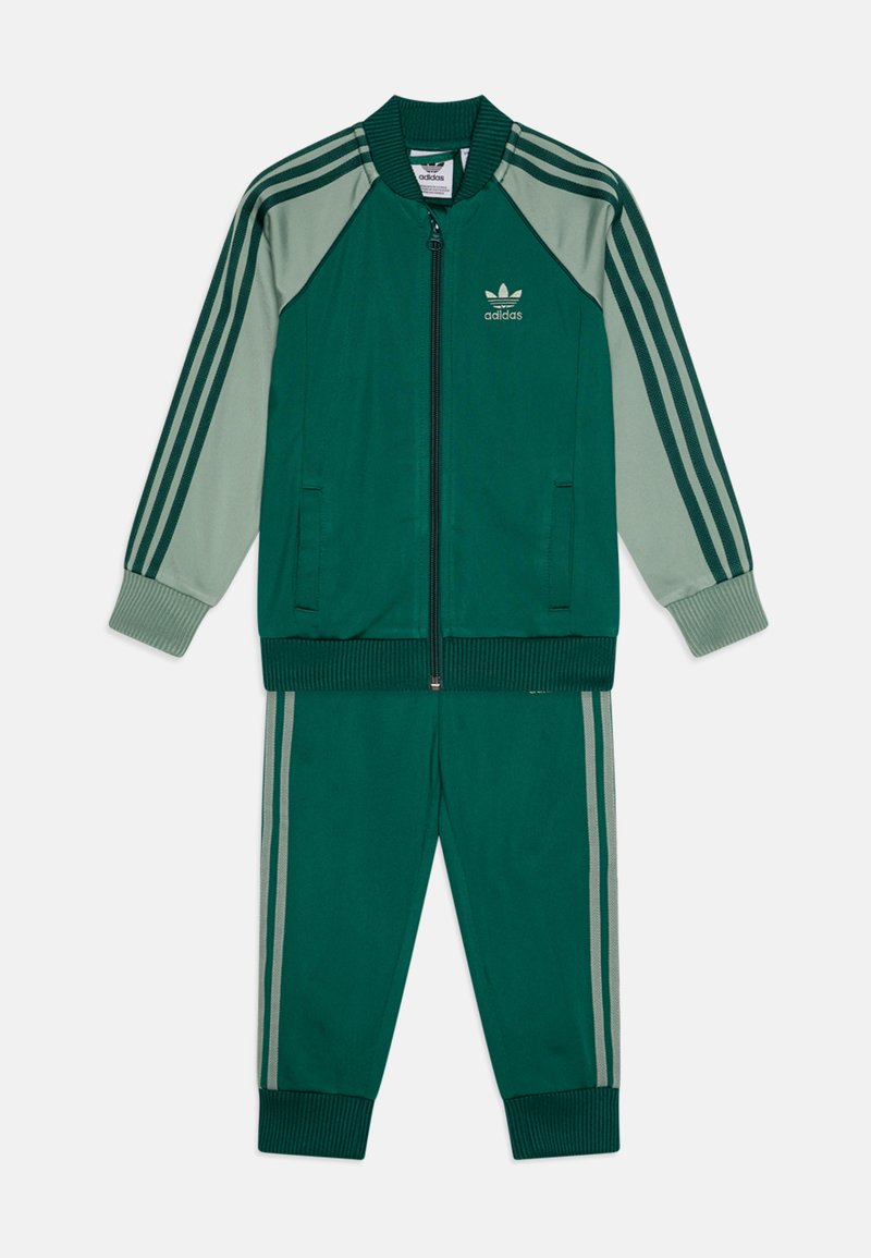 Σύνολο φόρμας σε σκούρο και ανοιχτό πράσινο, με περιλαίμιο φερμουάρ και ραμμένα μανίκια, καθώς και ταιριαστά παντελόνια με tapered γραμμή και πλευρικές ρίγες.