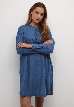 Denim-paitamekko, jossa on pyöreä kaula-aukko, pitkät hihat, etunapit ja sivurei'ät. Ominaisuuksia ovat rento istuvuus ja pehmeä rakenne keskisinisessä värissä.
