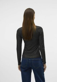 Zwarte geribbelde longsleeve top met een getailleerde silhouette, voorzien van een subtiele glans. Gecombineerd met donkerblauwe jeans, wat een casual stijl laat zien.