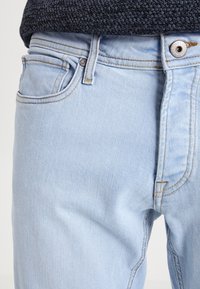 Jeans de mezclilla azul claro con un diseño clásico de cinco bolsillos, costuras en contraste y cierre de botón plateado. Textura suave, ajuste casual.