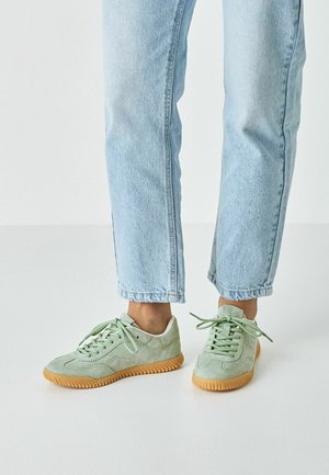 Mintgrønne ruskindssneakers med en tekstureret finish og gummisål, udstyret med runde snørebånd og et lavprofil-design. Bruges sammen med lyse denim-jeans.