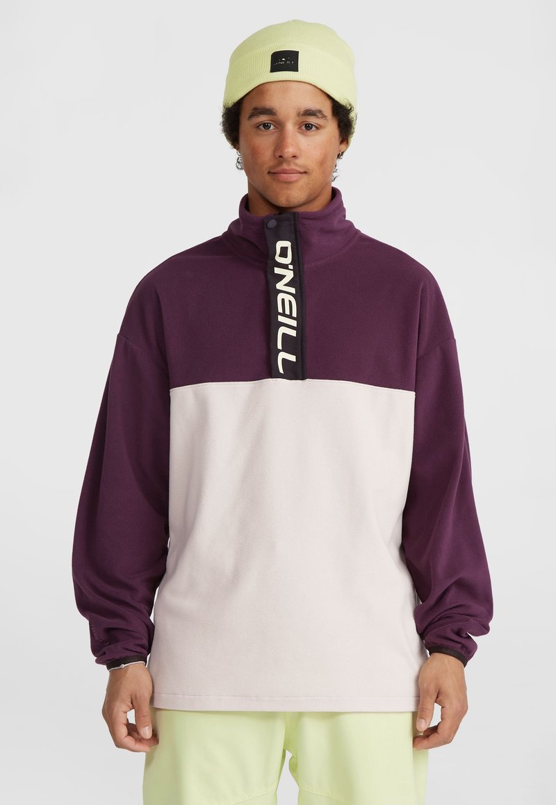 Pullover in pile con colletto alto, presenta una parte superiore viola e una parte inferiore bianca. Include un logo nero ben visibile sulla pattina della zip.