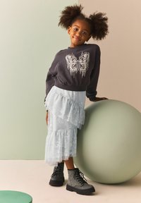 Sweatshirt gris avec un design de papillon, jupe en dentelle légère bleue empilée et bottes de combat noires scintillantes. Fond pastel doux.