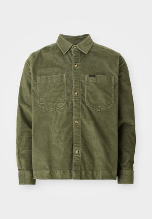 Camicia in corduroy verde con maniche lunghe, chiusura con bottoni frontale, due tasche sul petto e un piccolo etichetta sulla tasca sinistra.