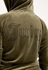 Olívazöld velúr kapucnis pulóver, amelynek hátulján nagy "Juicy" felirat található, fekete strasszokkal díszítve. Sima textúra és testhezálló kialakítás.