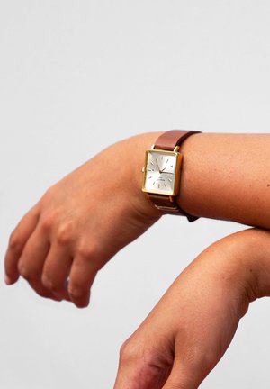 Montre avec bracelet en cuir marron, dotée d'un boîtier rectangulaire en or, d'un cadran blanc et d'aiguilles dorées avec de simples marqueurs horaires.