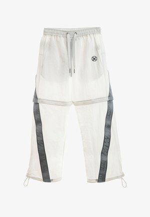 Pantalones casual blancos con cinturilla elástica, cordones, bolsillos delanteros, franjas laterales negras con texto y un pequeño logo redondo en el muslo izquierdo.