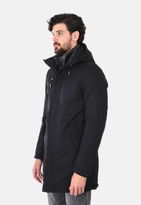 Giacca nera impermeabile con cappuccio, dotata di tasche con zip, maniche lunghe e taglio dritto. Tessuto liscio, design minimalista.