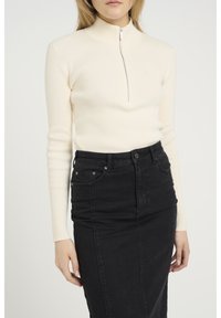 Maglione a costine cremoso con collo alto e zip a quarto, abbinato a una gonna a tubino in denim nera con tasche posteriori.