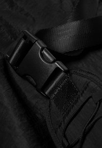 Black nylon strap with a plastic buckle. Textured surface and stitching visible. Includes elastic cord for adjustment.