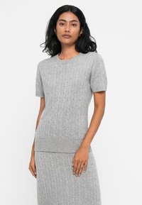 Maglione a maniche corte di colore grigio chiaro, realizzato in maglia con orlo a coste e motivo a trecce, realizzato in materiale morbido. Abbinato a una gonna a coste coordinata.