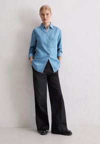 Jasnoniebieska koszula dżinsowa z długimi rękawami, z zapięciem na guziki z przodu, pojedynczą kieszenią na piersi, w zestawie z czarnymi, szerokimi spodniami o wysokim stanie i czarnymi butami.