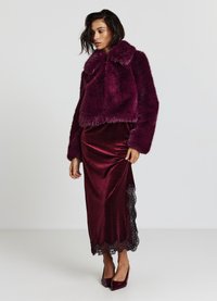 Veste en fausse fourrure bordeaux courte avec un large col, associée à une longue jupe en satin avec des bordures en dentelle noire à l'ourlet. Talons aiguilles bordeaux.