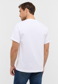 Biała bawełniana koszulka z krótkim rękawem, okrągłym dekoltem i luźnym krojem; jednolity wzór bez widocznych detali czy grafik.