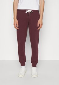 Burgundy sweatpants with a drawstring waist, tapered legs, and ribbed cuffs. Paired with white sneakers and a plain white T-shirt.