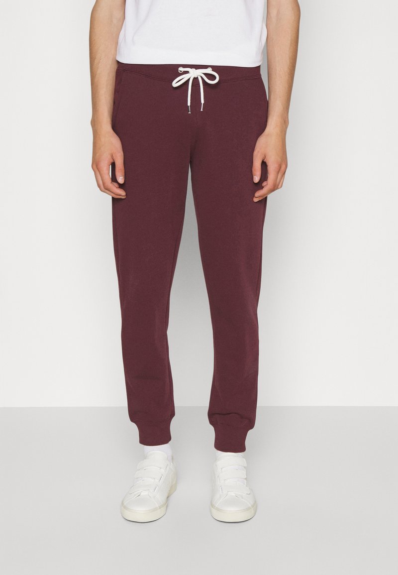 Burgundy sweatpants with a drawstring waist, tapered legs, and ribbed cuffs. Paired with white sneakers and a plain white T-shirt.