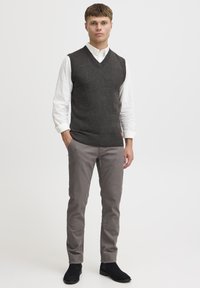 Grå strikket vest med V-udskæring, båret over en hvid skjorte med knapper. Grå slim-fit bukser og sorte ankelstøvler fuldender outfittet.