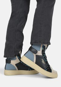High-top sneakers in gray, blue, and black with textile and leather materials, featuring a light-colored rubber sole and adjustable ankle strap.