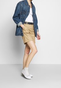 Jeansjacka med två bröstfickor, vit linne, khakishorts med uppvikta nederkant och vita högtoppsneakers.