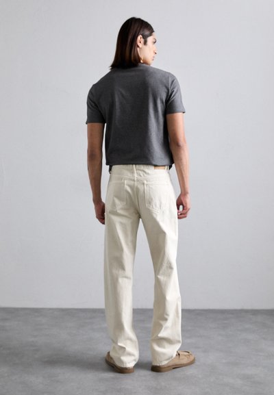 Grå kortermet t-skjorte kombinert med løstsittende hvite bukser, med en lett tekstur og synlige sømmer på baklommene.