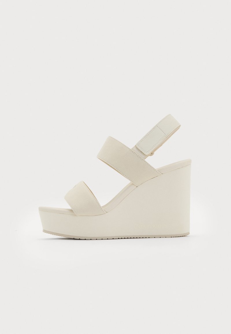 Sandale compensée beige avec deux larges brides sur le pied et une bride de cheville réglable avec fermeture à bande auto-agrippante.