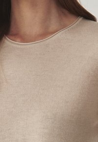 Beige gebreide sweatshirt met een ronde halslijn, gladde textuur en minimale naden, met een subtiele glans op de stof.