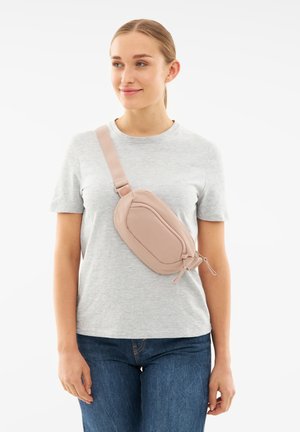 Rosa Kunstleder-Crossbody-Tasche mit schlankem Design, Reißverschluss und verstellbarem Tragegurt, getragen über einem grauen T-Shirt und blauen Jeans.