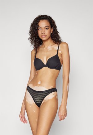 Juodas paminkštintas liemenėlė su reguliuojamais petnešėlėmis ir atitinkančiais juodais kelnaitėmis, dekoruotomis logotipo raštu. Lygi tekstūra ir prigludusi forma.