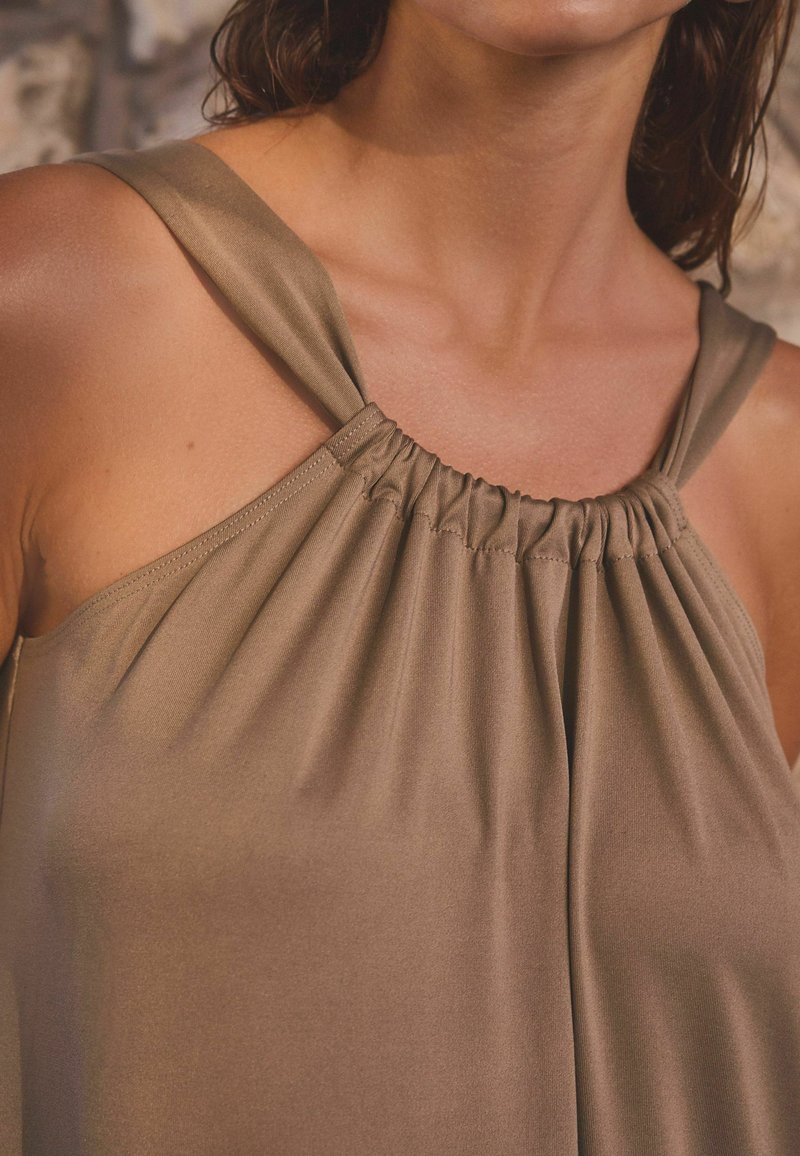 Haut marron sans manches en tissu lisse. Présente des détails froncés au niveau de l'encolure et des bretelles larges. Coupe simple et décontractée.