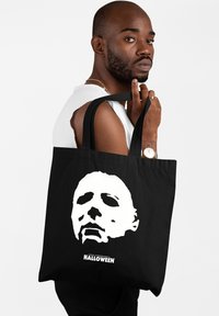 Czarna torba tote z dużą białą grafiką zamaskowanej twarzy oraz napisem "HALLOWEEN JOHNA CARPENTERA" na dole. Wytrzymały materiał, miękka faktura.