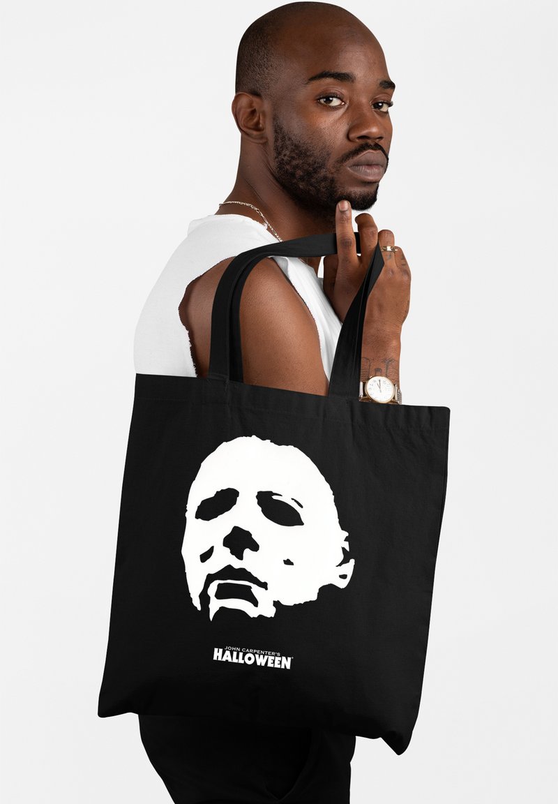 Czarna torba tote z dużą białą grafiką zamaskowanej twarzy oraz napisem "HALLOWEEN JOHNA CARPENTERA" na dole. Wytrzymały materiał, miękka faktura.