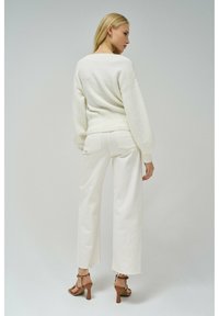 Maglione bianco, struttura testurizzata, con vestibilità ampia e orlo a coste, abbinato a pantaloni bianchi a gamba larga a vita alta e sandali marroni con tacco.