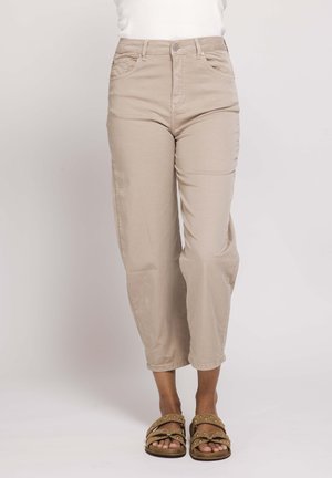 Person wearing beige high-waist straight-leg pants paired with studded tan double-strap sandals standing against a plain background.