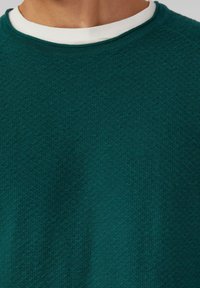 Teal kleurige gebreide trui met een ronde hals, voorzien van een subtiel ruitpatroon en een contrasterende witte binnenkraag. Zachte stof, casual ontwerp.