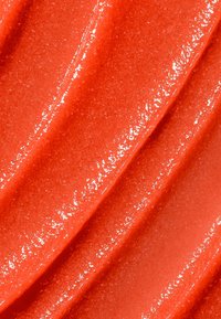 Crema cosmetica rosso brillante con una texture lucida, che mostra motivi ondulati e lisci con una finitura scintillante.
