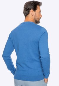 Blauer Rundhalsausschnitt-Pullover mit langen Ärmeln und geripptem Saum. Der Stoff wirkt glatt und gestrickt und zeigt eine gleichmäßige Textur.