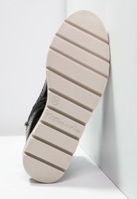Suela de zapato negra con surcos horizontales, de goma de color claro, y la marca "Tamaris" grabada. Talla marcada como 36.