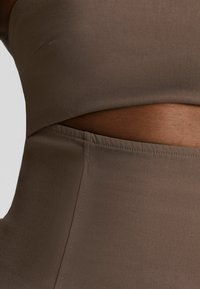 Gros plan sur un ensemble de sport marron sans couture mettant en valeur un bas taille haute et un haut court sur un corps à la peau foncée.