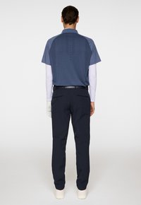 Heren golfoutfit met een blauwe polo met korte mouwen en marineblauwe broek. Bevat een gestructureerd ontwerp aan de achterkant en een riem voor een strakke look.