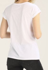 Camiseta de algodón blanca con mangas enrolladas, escote redondo y un corte holgado. La tela parece suave con una textura lisa. Diseño sencillo.