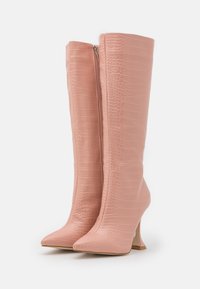 Wysokie różowe buty z teksturą krokodyla, ze spiczastymi noskami, bocznymi zamkami i wysokimi zakrzywionymi obcasami skierowanymi do wewnątrz.